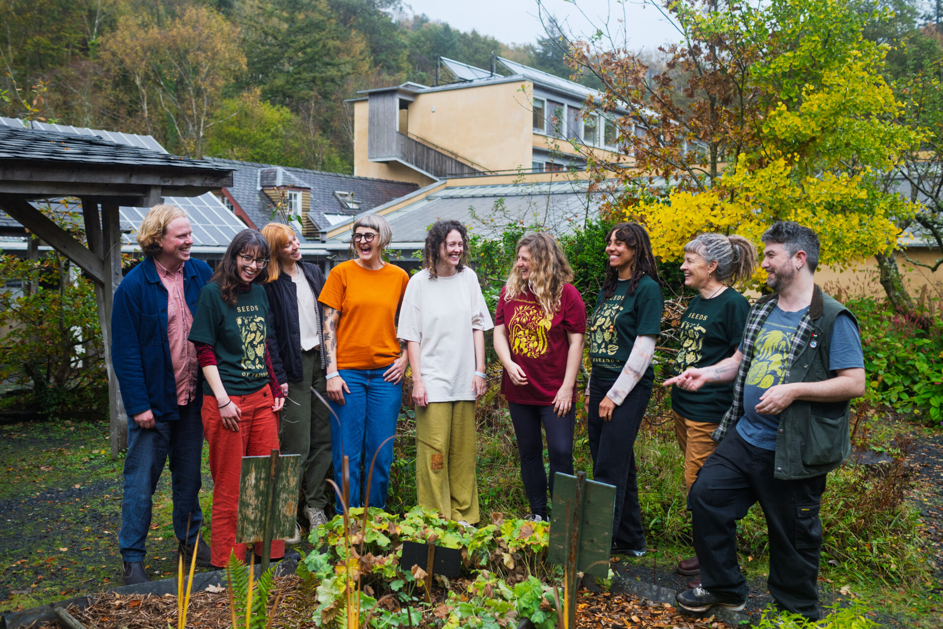 Group of seed sovereignty practitioners gathered in garden setting with buildings and autumn trees